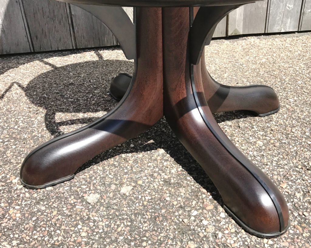 Close-up of the dark wooden base of a bar stool with four curved feet, standing on a textured outdoor surface, sunlight and shadow visible—perfectly paired with bespoke bar stools for stylish outdoor gatherings.
