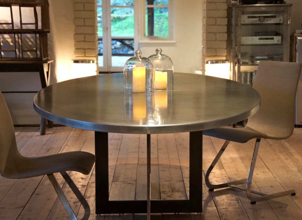 An oval zinc-topped table with two glass-covered candles sits between two modern beige chairs in a cosy room with wooden floors and soft lighting.