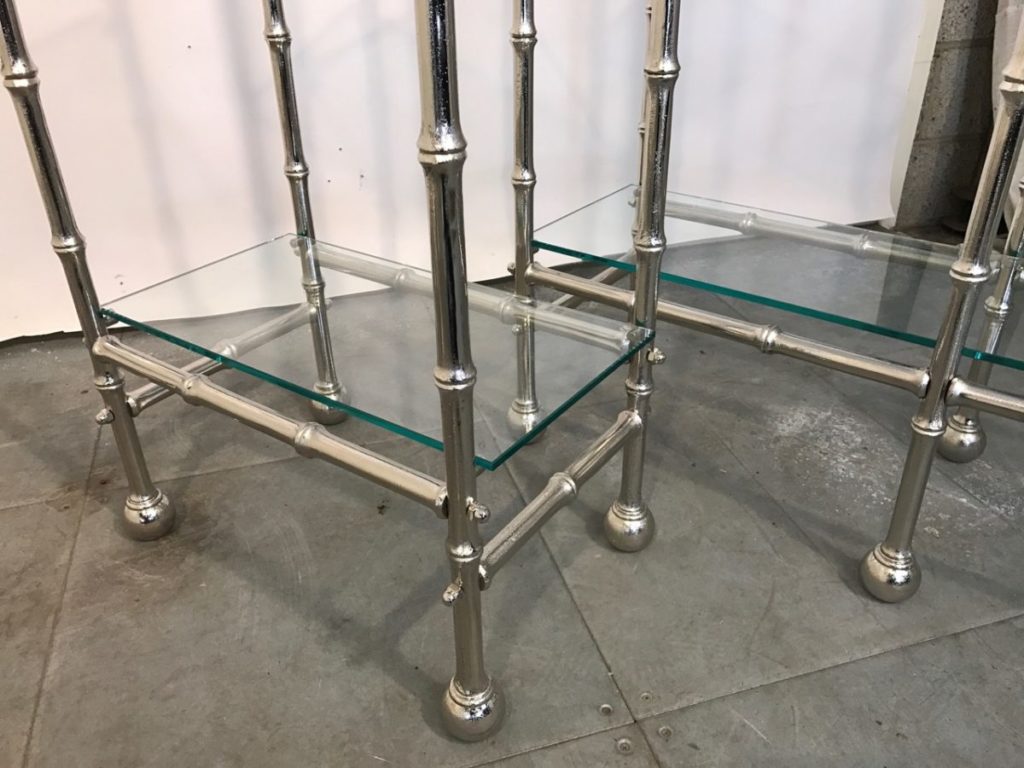 A close-up view of glass shelves, with solid brass étagères, featuring legs designed to look like bamboo stalks and standing on a grey tiled floor.