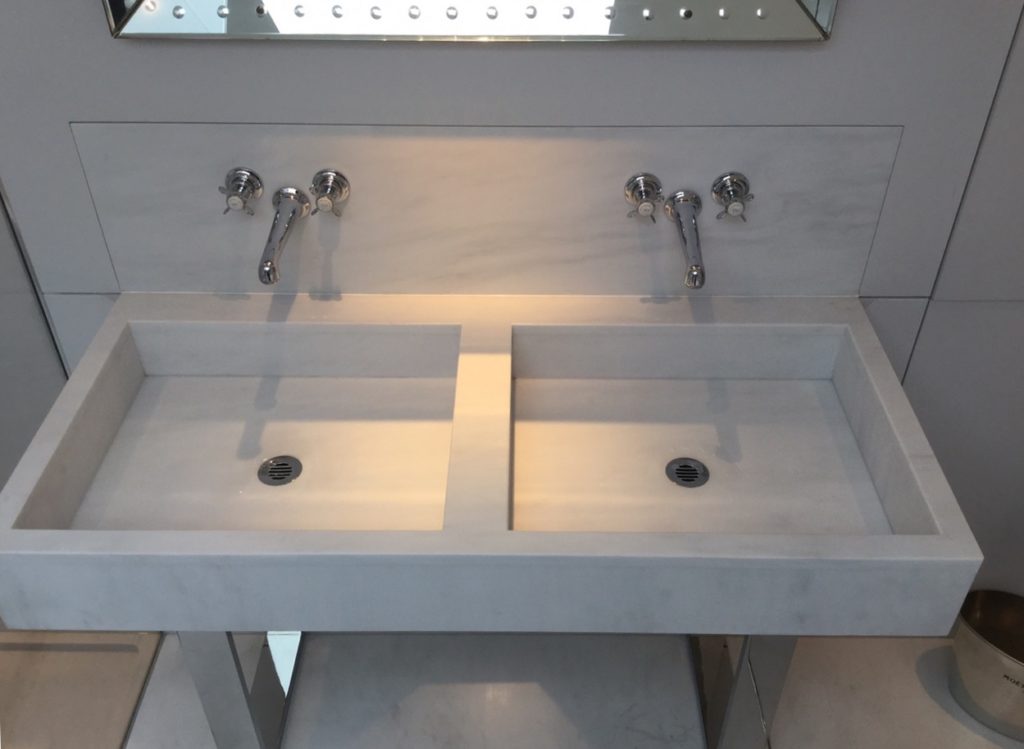 A modern bespoke bathroom washstand featuring two rectangular basins and wall-mounted faucets in a sleek, light gray finish, set beneath a mirror.