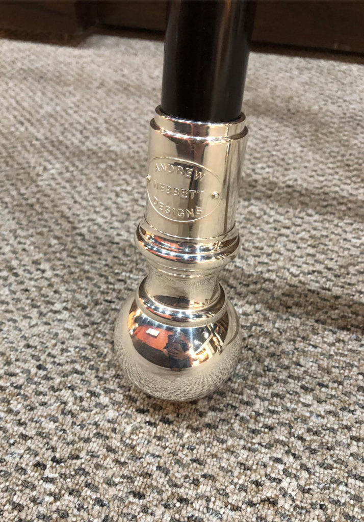 A close-up of the silver foot of a black library ladder, engraved with Andrew Nebbett Designs, resting on a beige carpet.