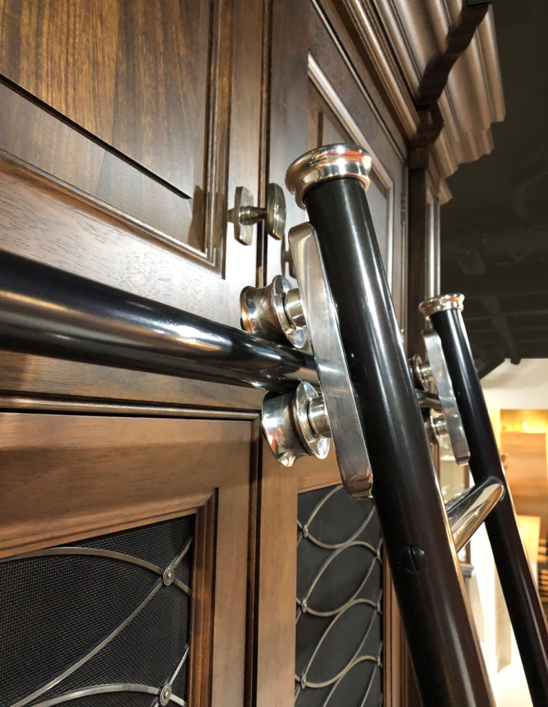 Close-up of a black rolling library ladder attached to a dark wooden bookcase with silver fittings and ornate details.