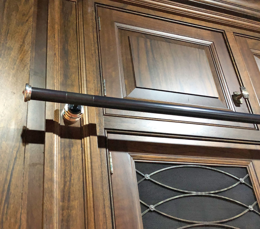 A dark brown library ladder rail with metallic ends is loosely mounted above a decorative wooden door with raised panels and ironmongery detailing, reminiscent of doors often paired with a rolling library ladder.