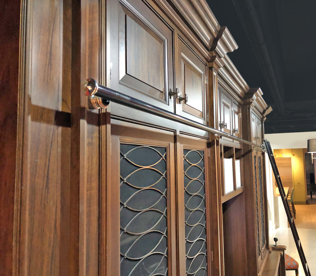 A close-up of tall wooden cupboards with decorative glass doors and a polished metal library ladder rail for a rolling library ladder, in a well-lit interior space.