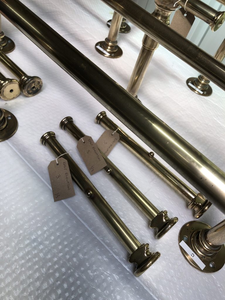 Metal pipes and fixtures are laid out on bubble wrap, ready for assembly. Three pipes have labeled tags attached to them, hinting at their role in crafting bespoke dressing room furniture. The pipes and fixtures boast a shiny brass finish that exudes elegance and sophistication.