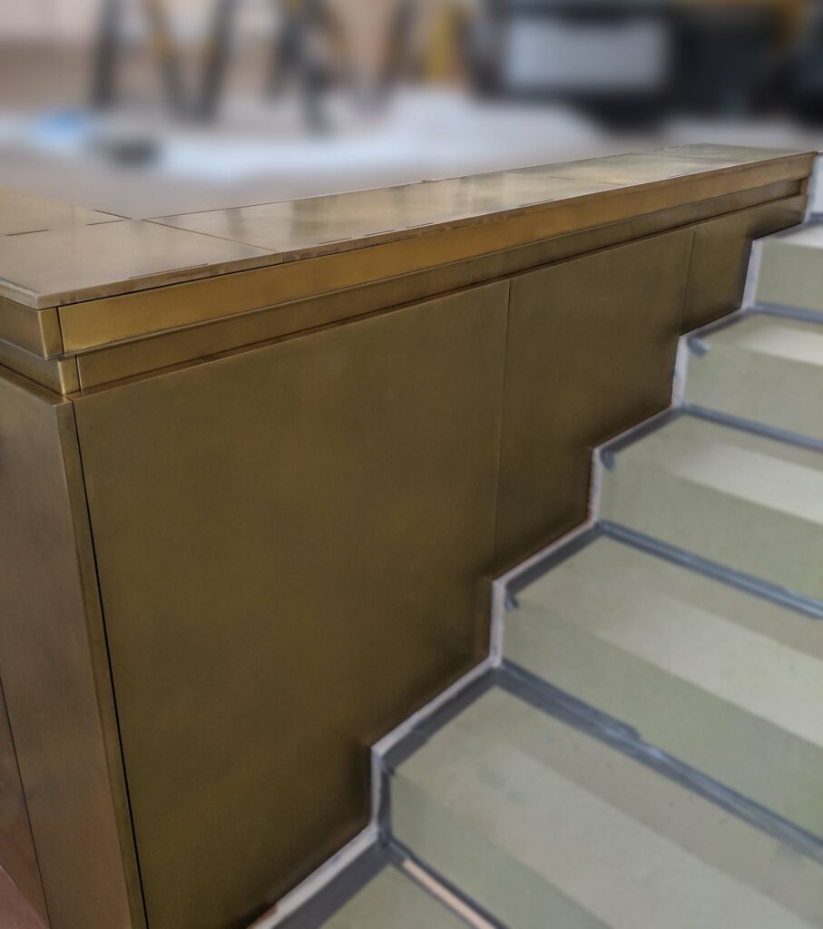 A modern staircase with light-colored steps bordered in darker material is accentuated by elegant wall paneling. Adjacent to the stairs is a sleek, metallic structure with a flat top and minimalist design, enhancing the contemporary aesthetic.