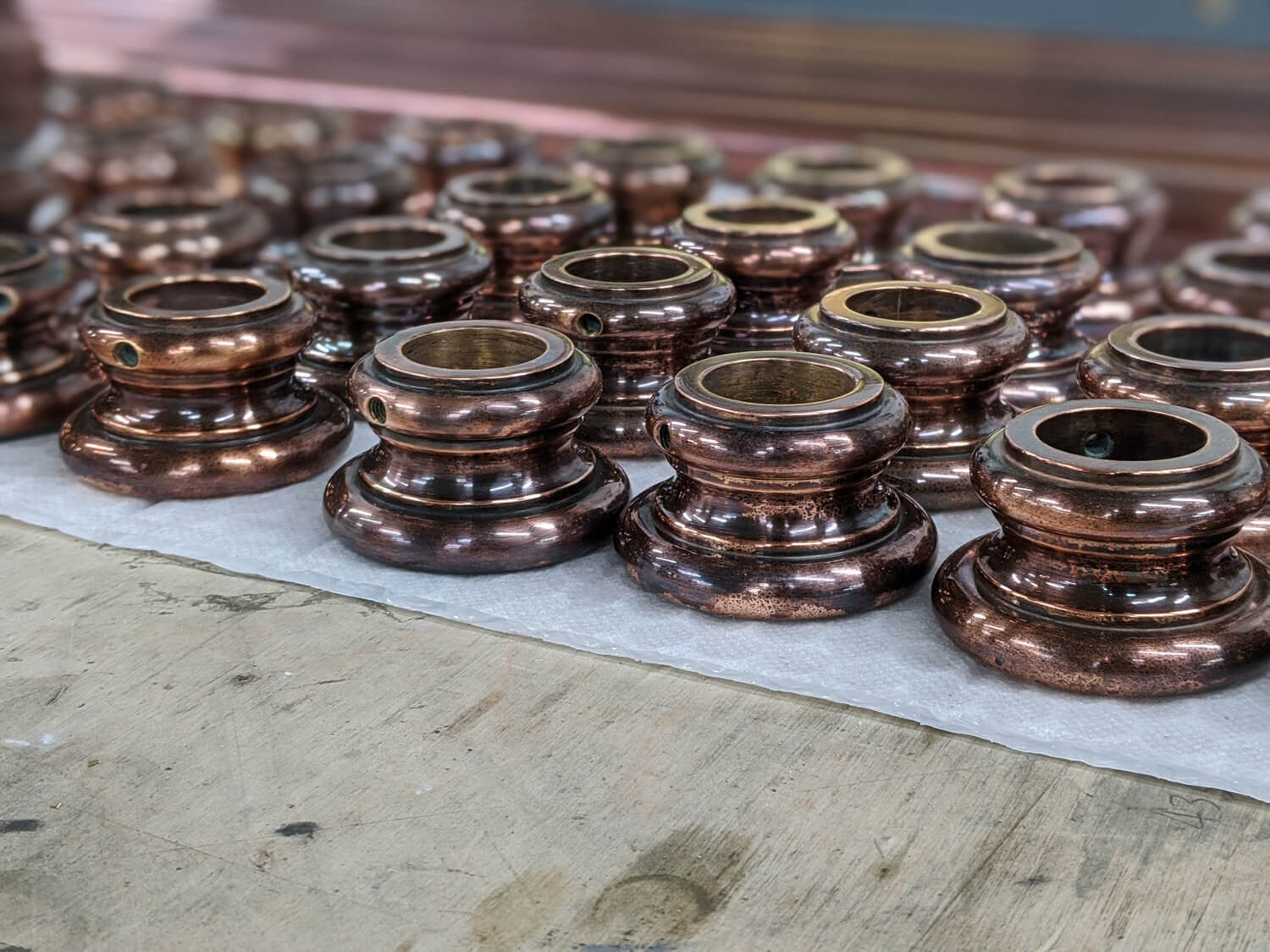 A collection of polished copper plated metal fittings arranged neatly on a wooden surface, with a focus on their shiny, reflective surfaces and cylindrical shapes.