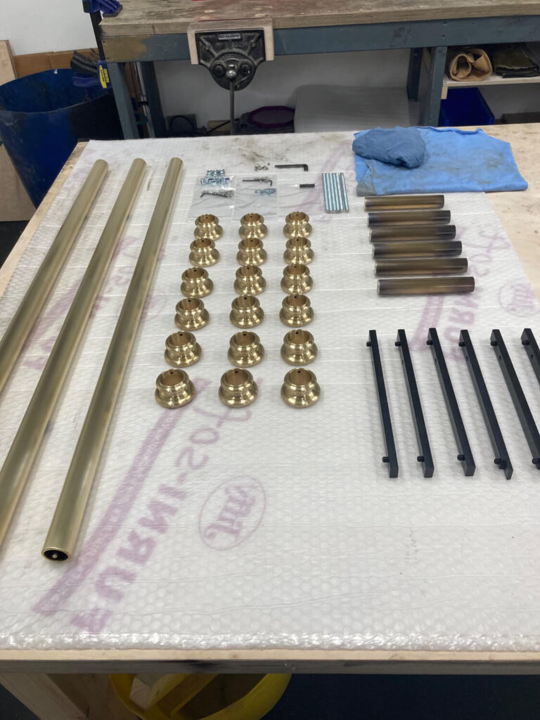 Brass rods, round brass fittings, black handles, screws, brass rods, and blue cloth laid out neatly on a bubble-wrapped table in a workshop.