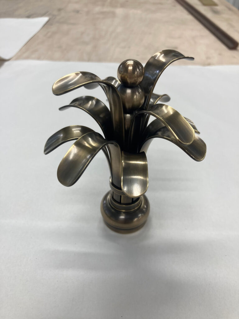 brass shelf finals in the shape of palm trees, placed on a white surface with a wooden background.