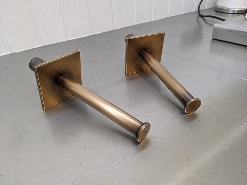 Two bronze wall-mounted valet rods with square bases rest on a gray countertop.