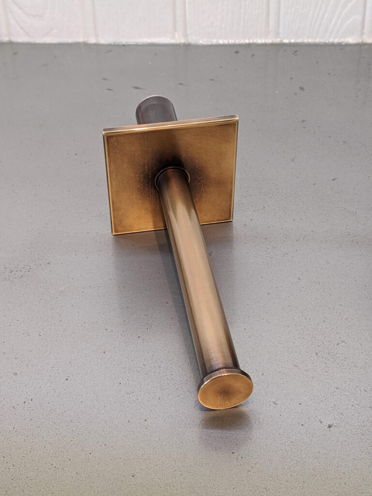 A brass wall-mounted rod with a square base plate resting on a gray countertop.