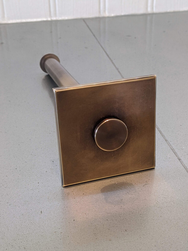 A retractable valet rod with a square base is resting on a gray zinc worktop against a white wall.