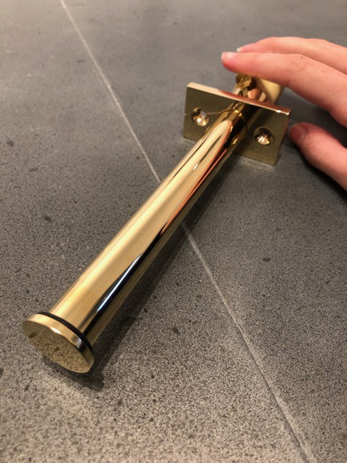 A hand holding a shiny brass valet hook.