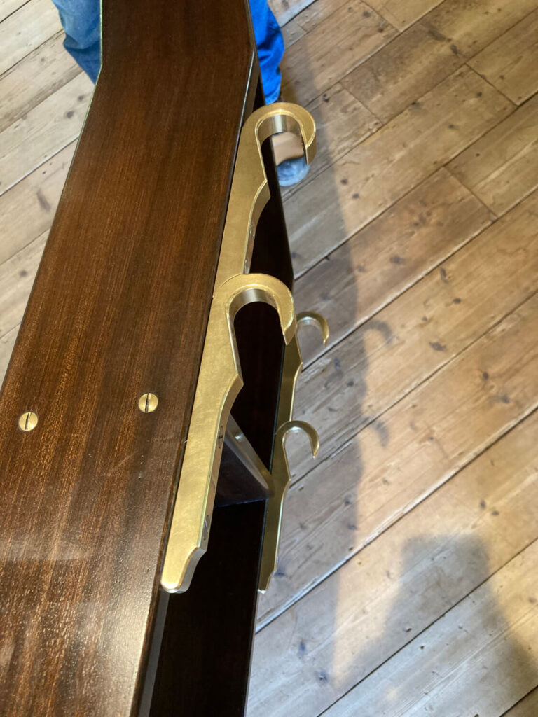Two brass hooks are attached to the edge of a dark wooden ladder.