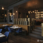 Elegant restaurant interior with modern décor, featuring blue chairs, brown leather booths, neatly set tables, pendant lights, and a softly lit raised dining area with a brushed brass balustrade.