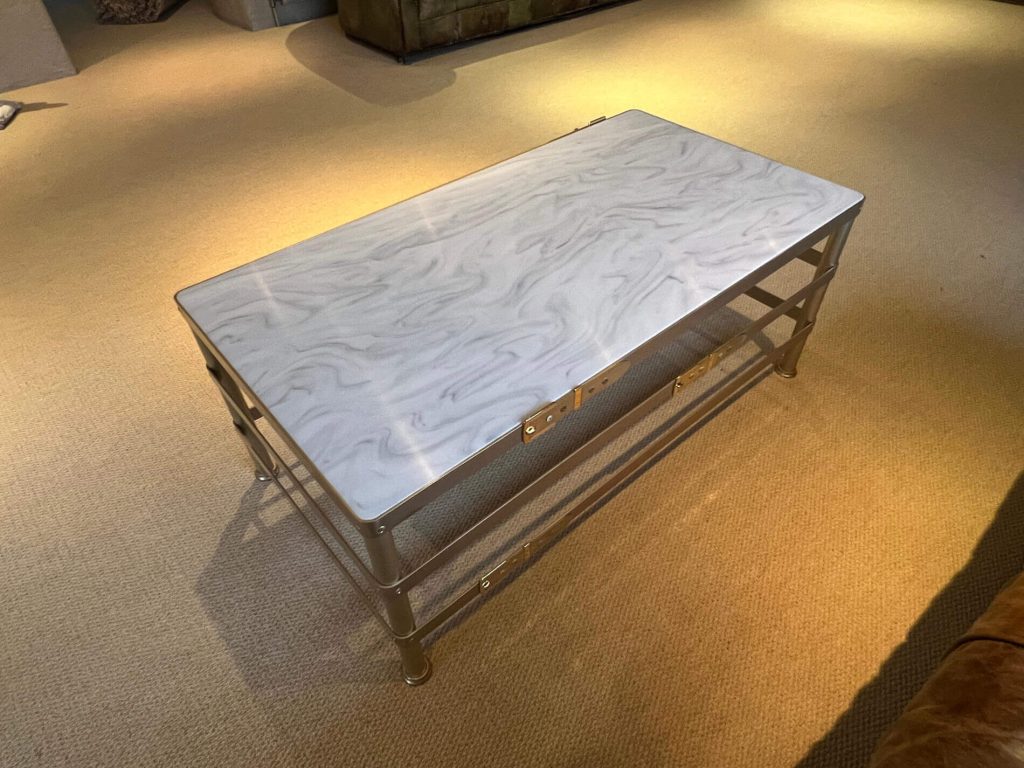 Rectangular coffee table with a white, marble-like top and a metallic frame, placed on a light beige carpet in a warmly lit room.