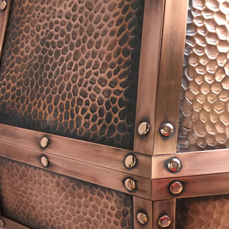 Close-up of a textured, hammered metal surface with a bronze finish, its a classic copper surfacee, framed and accented by smooth metal strips secured with round rivets at the intersections.